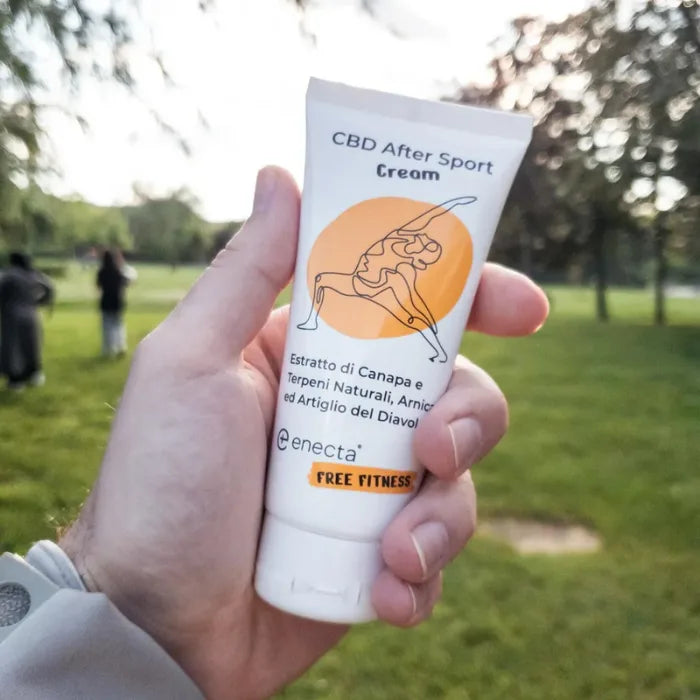 Enecta CBD Muskelbalsam mit 700 mg CBD, 100-ml-Tube mit Yoga-Motiv wird in einer Hand vor einer Parkwiese gehalten